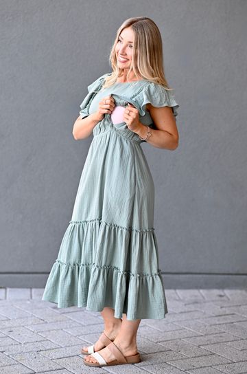 A breastfeeding mom wearing a 100% cotton nursing dress in a green color with sandals 