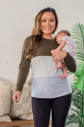 Woman holding a baby in a room with a plant and furniture wearing a nursing shirt