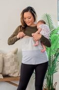 Woman holding a baby in a room with a plant and pillows. She is wearing a green nursing shirt. 
