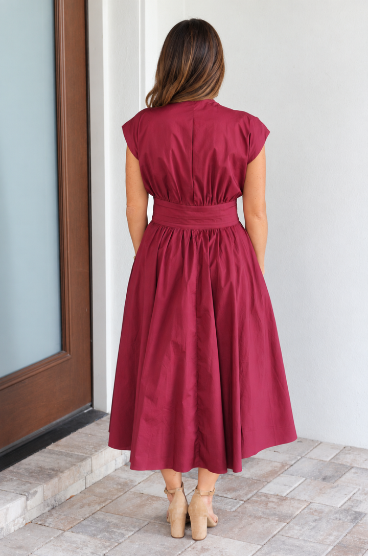 Back view of a mom wearing a red cotton nursing dress with pockets standing on the front porch