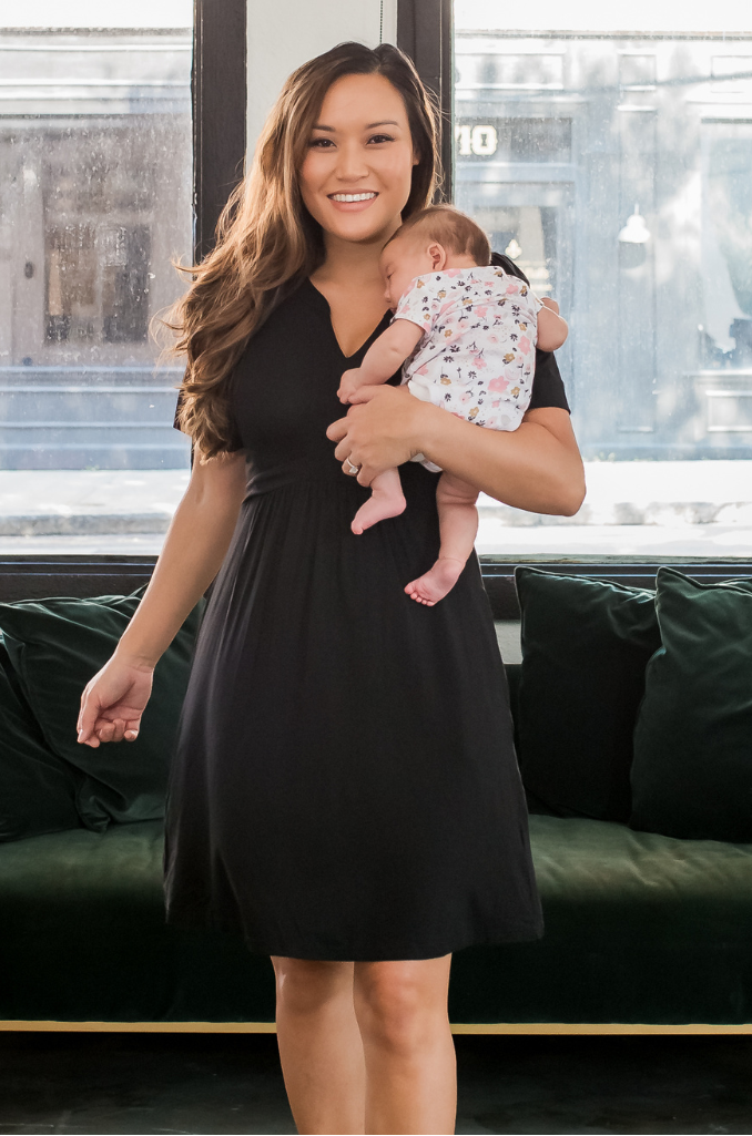 Woman in a black short sleeve nursing dress holding a baby in a modern living room. 