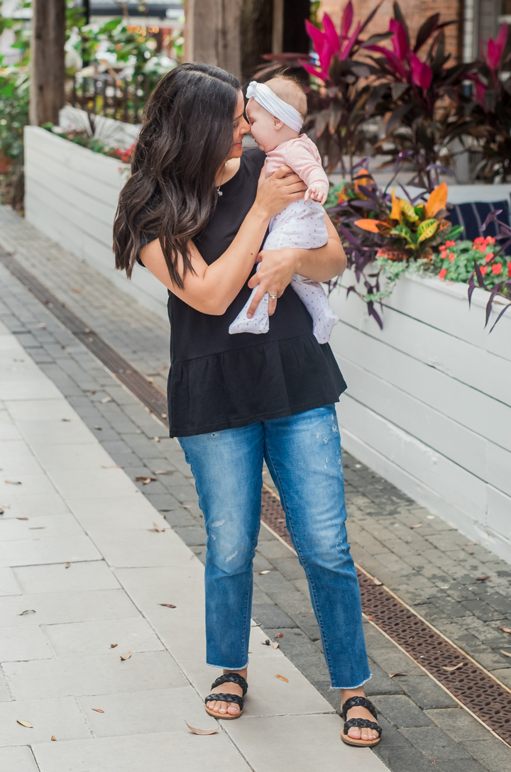 Breastfeeding mom holding a baby while wearing a black cotton nursing top with ruffle detail.