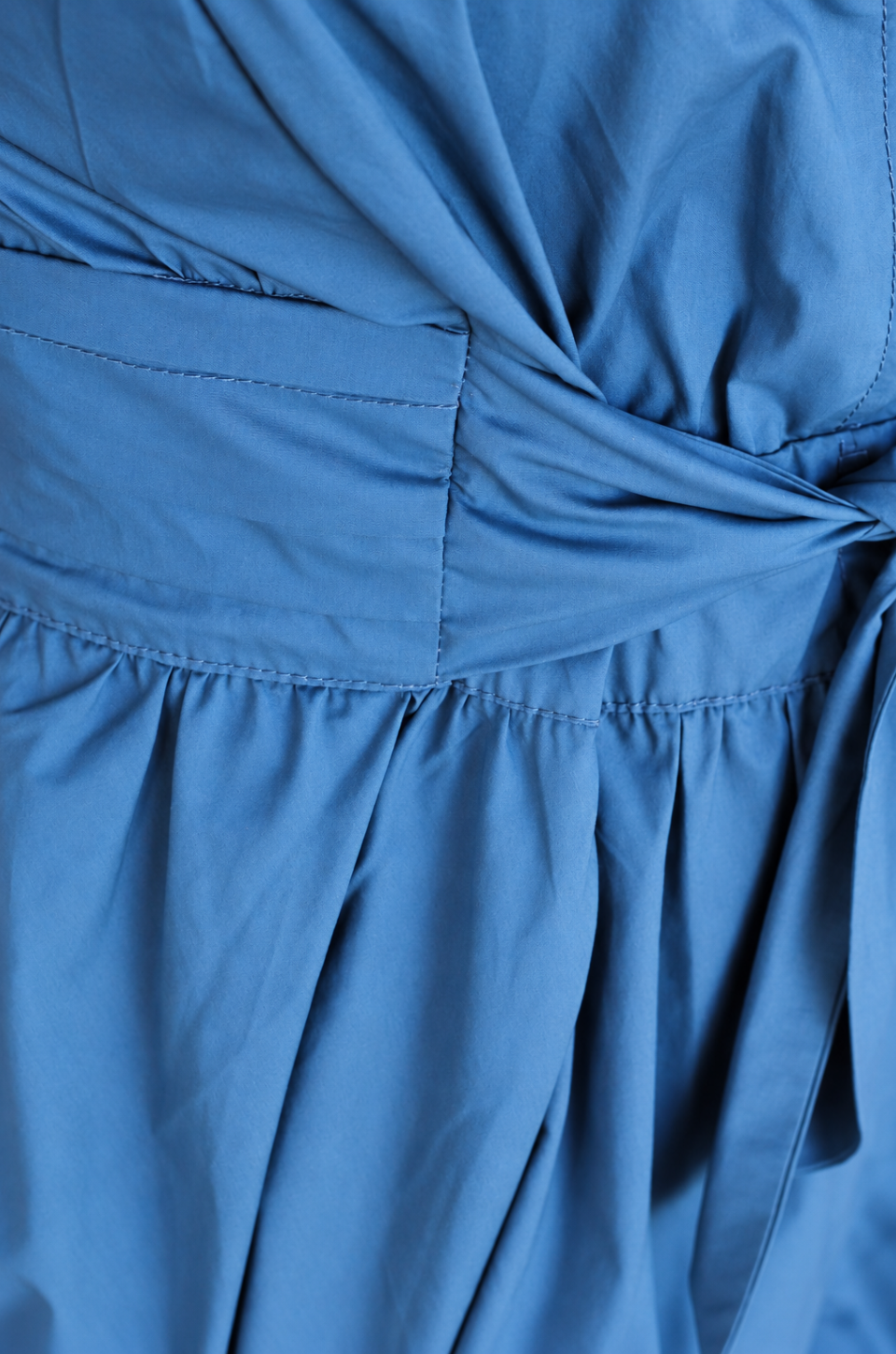 Close-up of a blue fabric garment showing gathered pleats and a twisted waist detail.