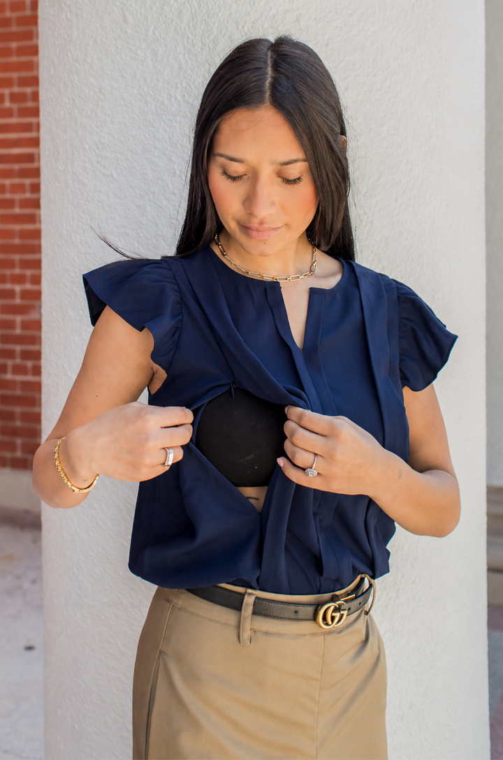 Woman wearing a navy blue nursing top against a light-colored wall.