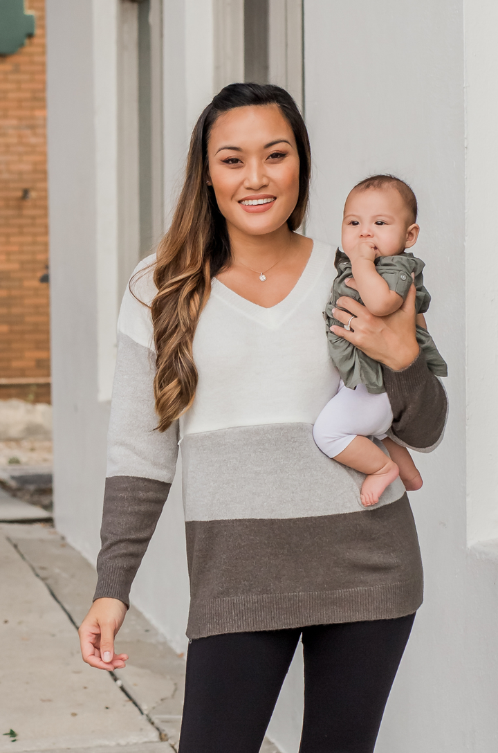 Front view of breastfeeding mom wearing gray colorblock fuzzy nursing sweater while holding a baby, showing V-neckline and concealed nursing access.