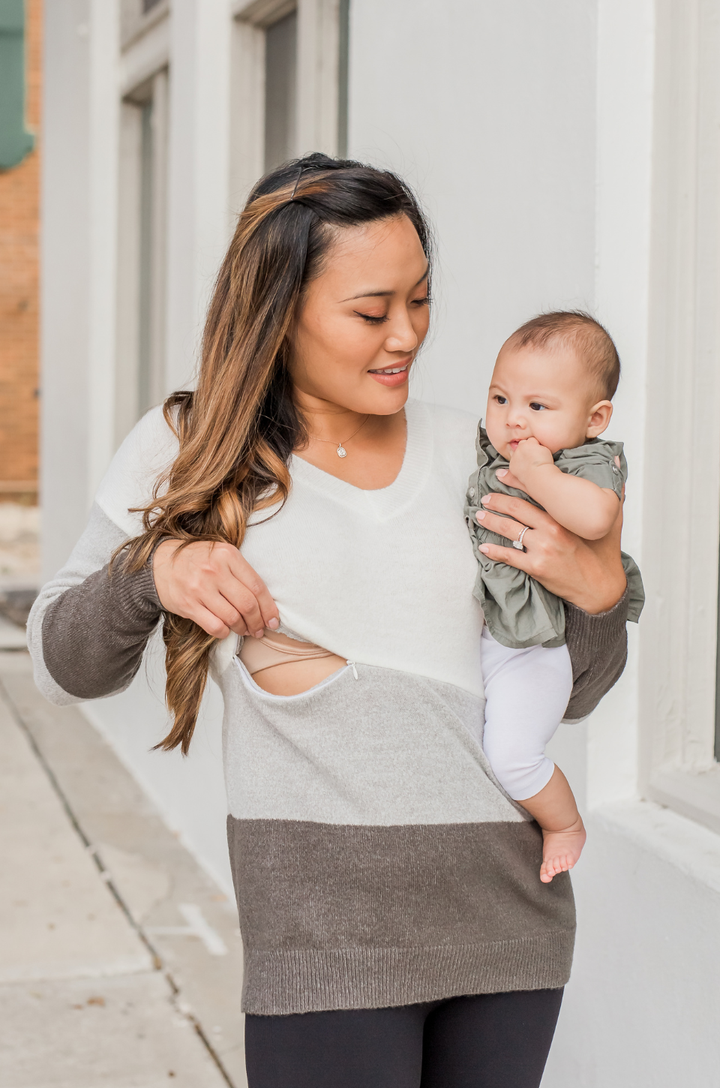 Front view of breastfeeding mom wearing gray colorblock fuzzy nursing sweater while holding a baby, with concealed nursing access. 