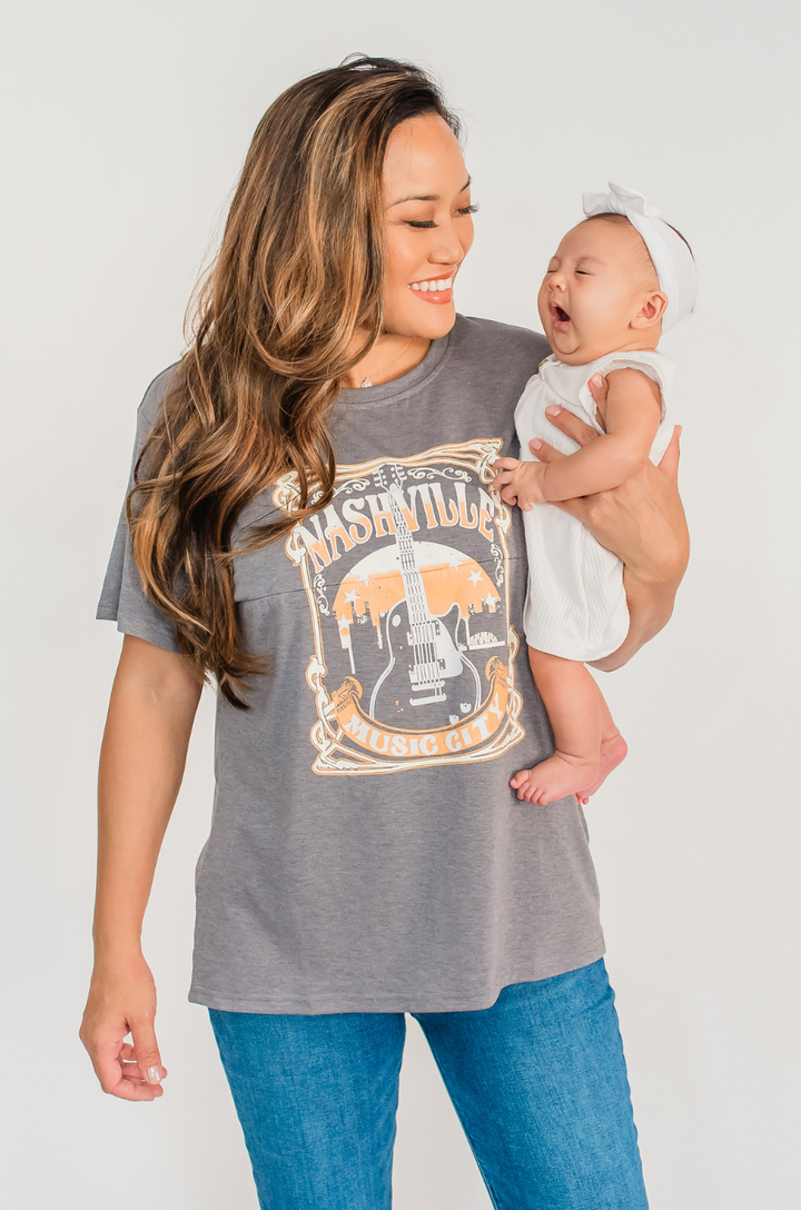 A mom wears the Nashville nursing graphic gray t-shirt from Nursing Queen paired with jeans for a comfortable, everyday outfit.