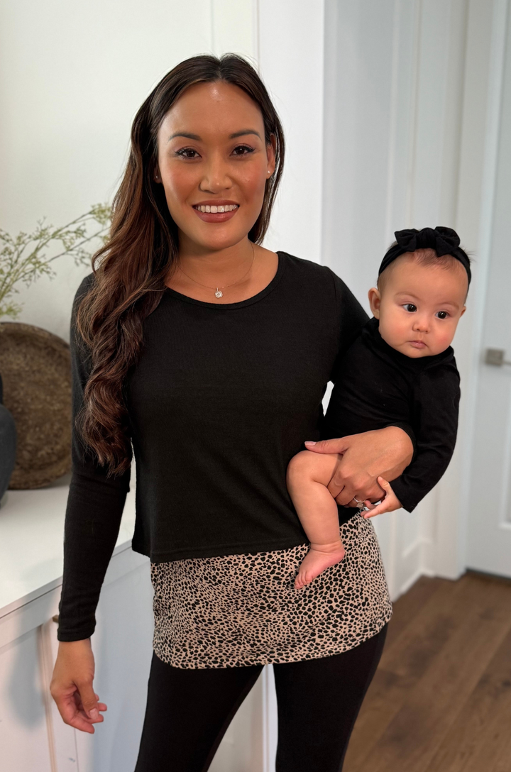 Front view of mom wearing the black leopard print double layer nursing sweater while holding a baby, showing layered breastfeeding access.