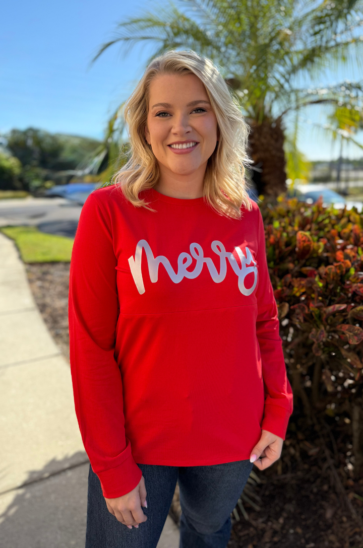 Woman wearing a red long sleeve nursing top that says Merry on the front. 