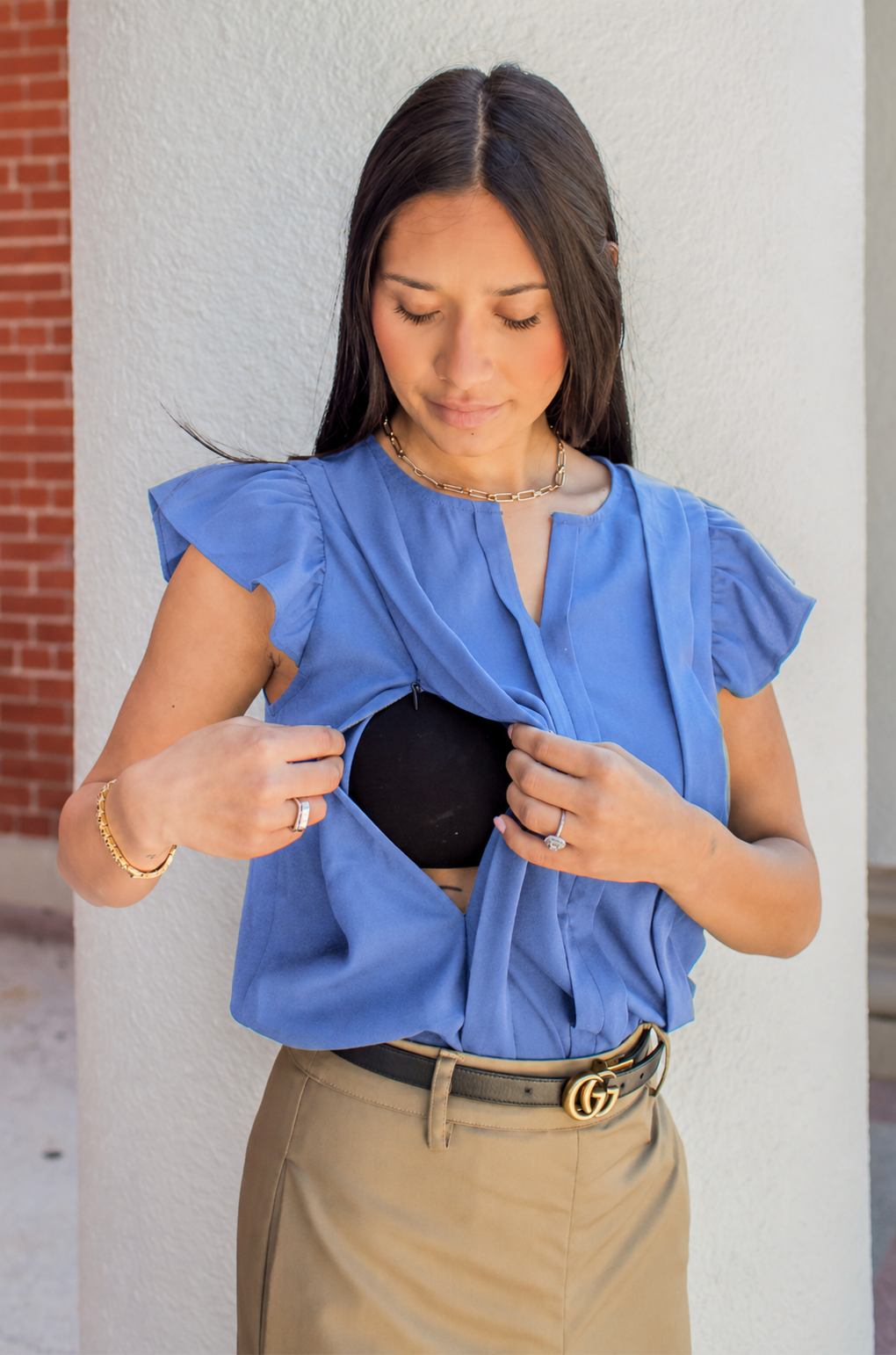 Woman wearing a blue nursing top standing against a light-colored wall.