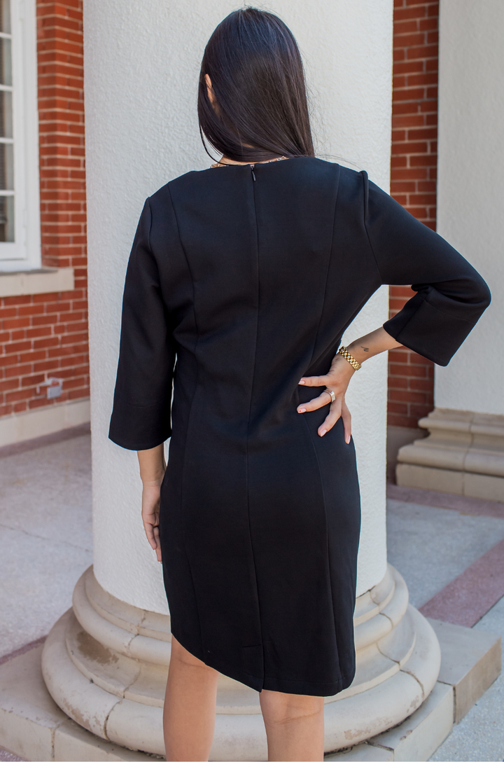 Back view of a woman wearing a black maternity and nursing dress with hidden breastfeeding access. 