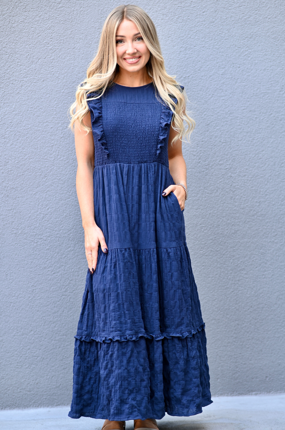 Woman wearing a blue cotton nursing dress, standing in front of a gray background