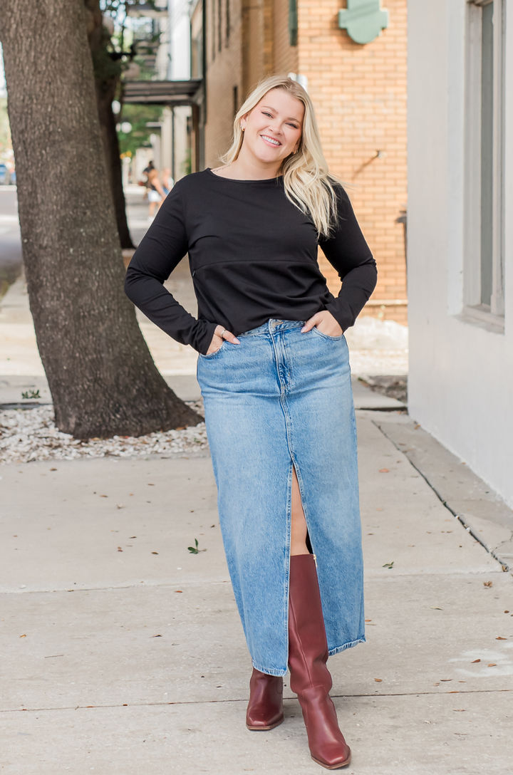 Front view of breastfeeding mom wearing black long sleeve cotton nursing top styled with a jean skirt and maroon boots, showing concealed zipper nursing access.
