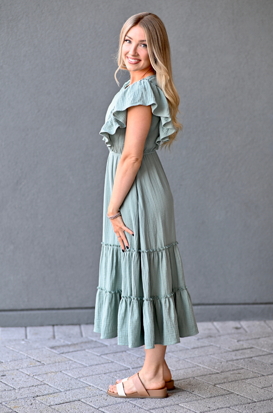 Woman wearing a seafoam nursing dress with ruffled sleeves and bottom hem against a gray background