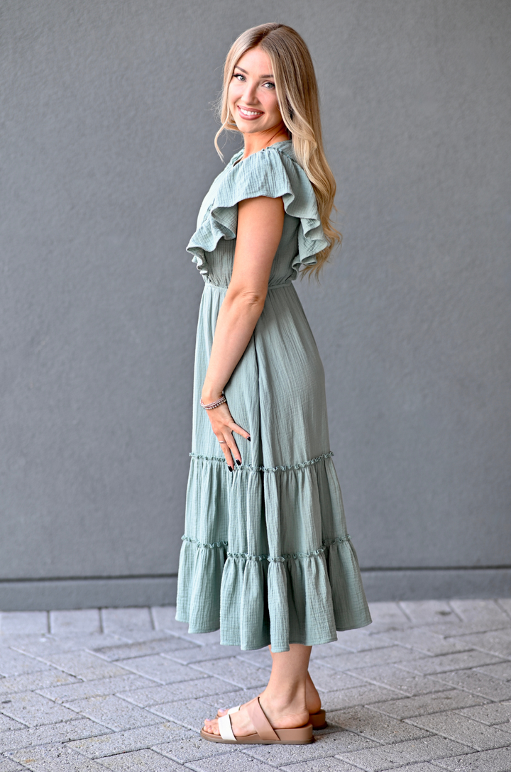 Woman wearing a seafoam nursing dress with ruffled sleeves and bottom hem against a gray background