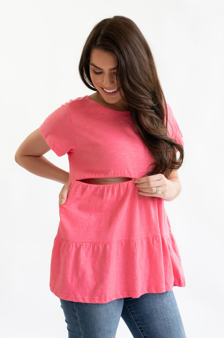 Breastfeeding mom wearing a pink cotton nursing top with ruffle detail, showing hidden nursing access opened at the front.