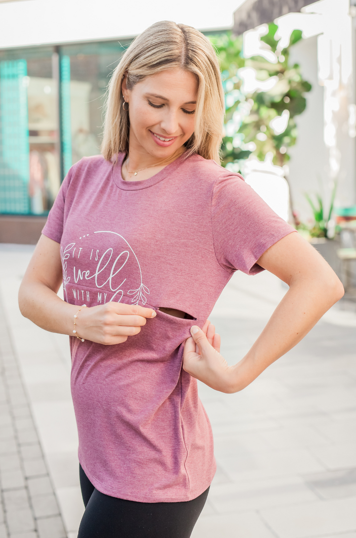 Mom wearing a heather plum nursing shirt with the breastfeeding access partially open. 
