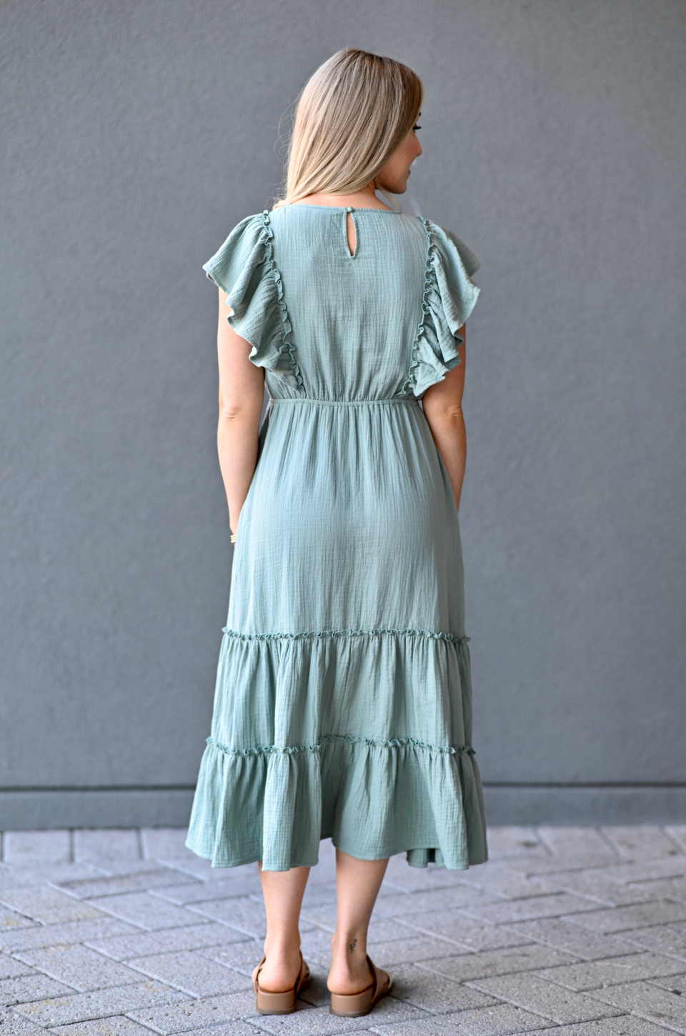 Woman wearing a seafoam breastfeeding dress with ruffled sleeves and bottom hem against a gray backdrop.