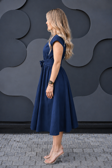 A woman wearing a navy blue cotton midi breastfeeding dress with a tie waist