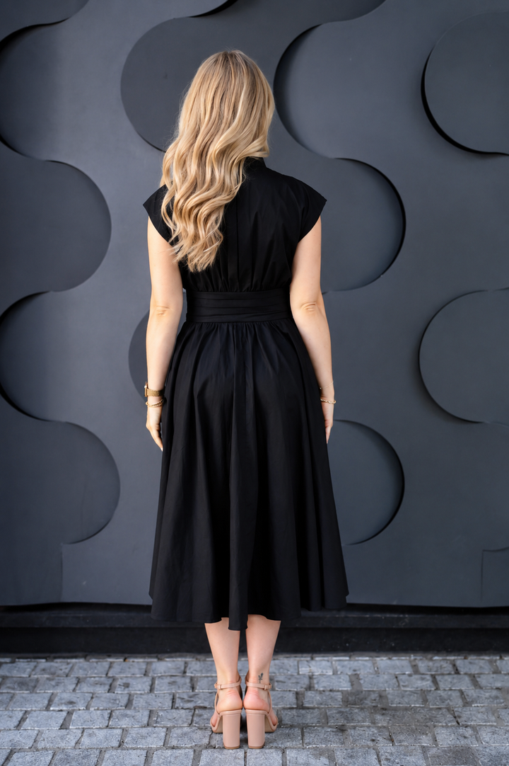 A woman viewed from behind wearing a black midi cotton nursing dress with cap sleeves and a defined waist