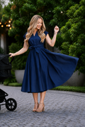 A woman wearing a navy blue nursing midi dress with a tie waist and V-neckline with stroller