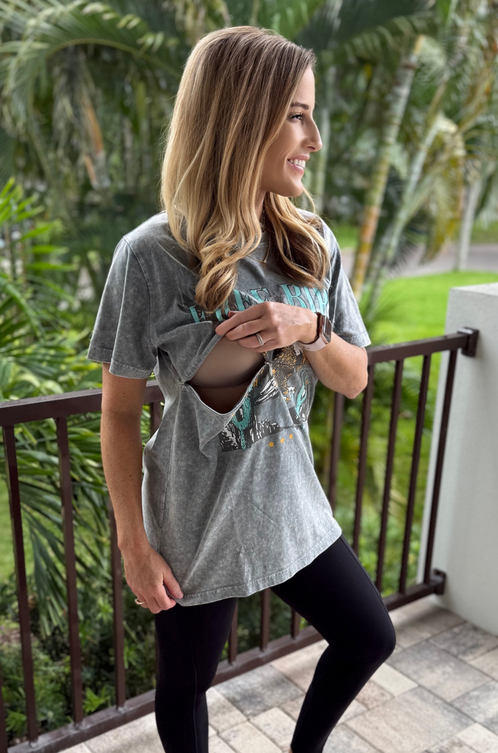 A mom opens the hidden breastfeeding access on the Free Bird graphic stonewash gray tee from Nursing Queen to nurse or pump comfortably.