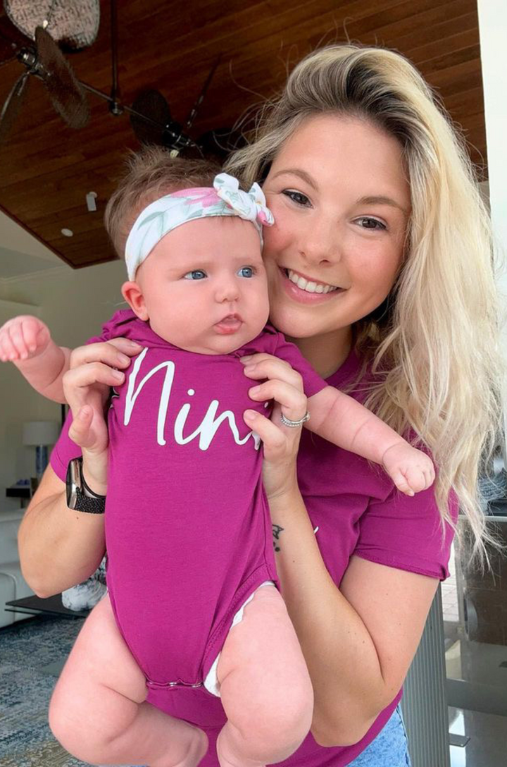 Close-up of cursive “mini” text on matching baby onesie.