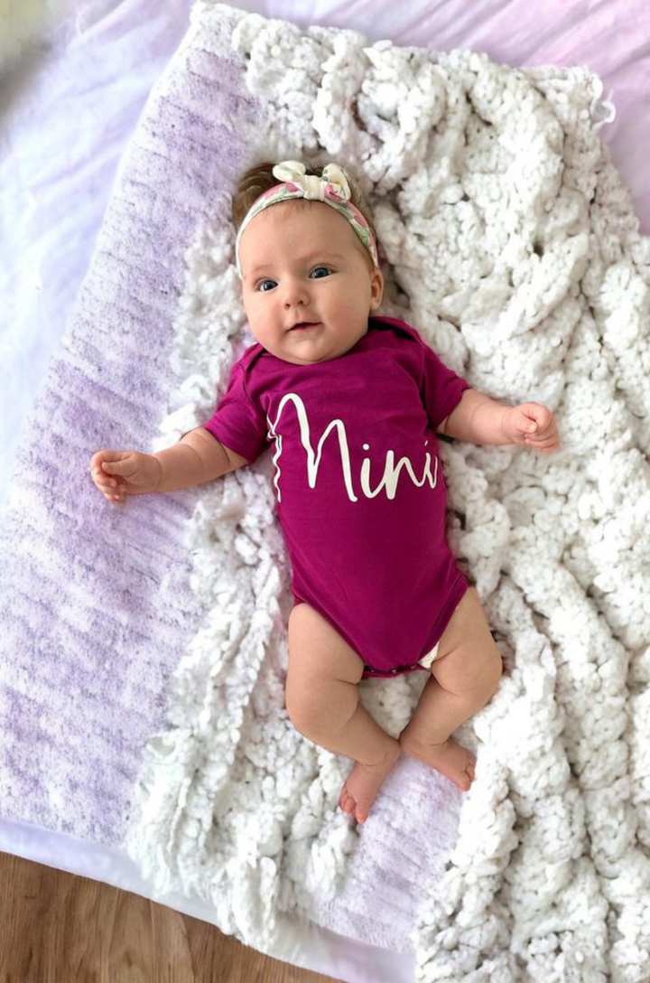 Close-up of cursive “mini” text on matching berry baby onesie. 