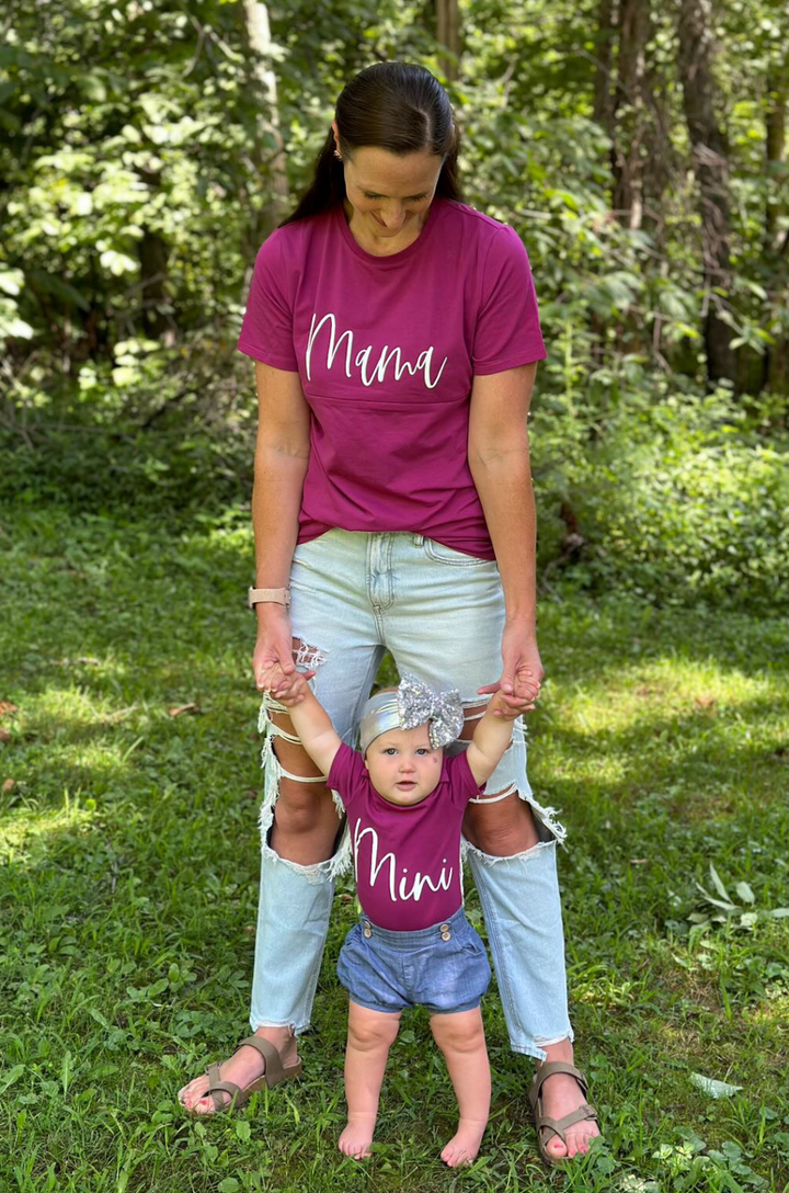 Breastfeeding mom and baby wearing matching berry T-shirts with cursive “mama” and “mini” text.