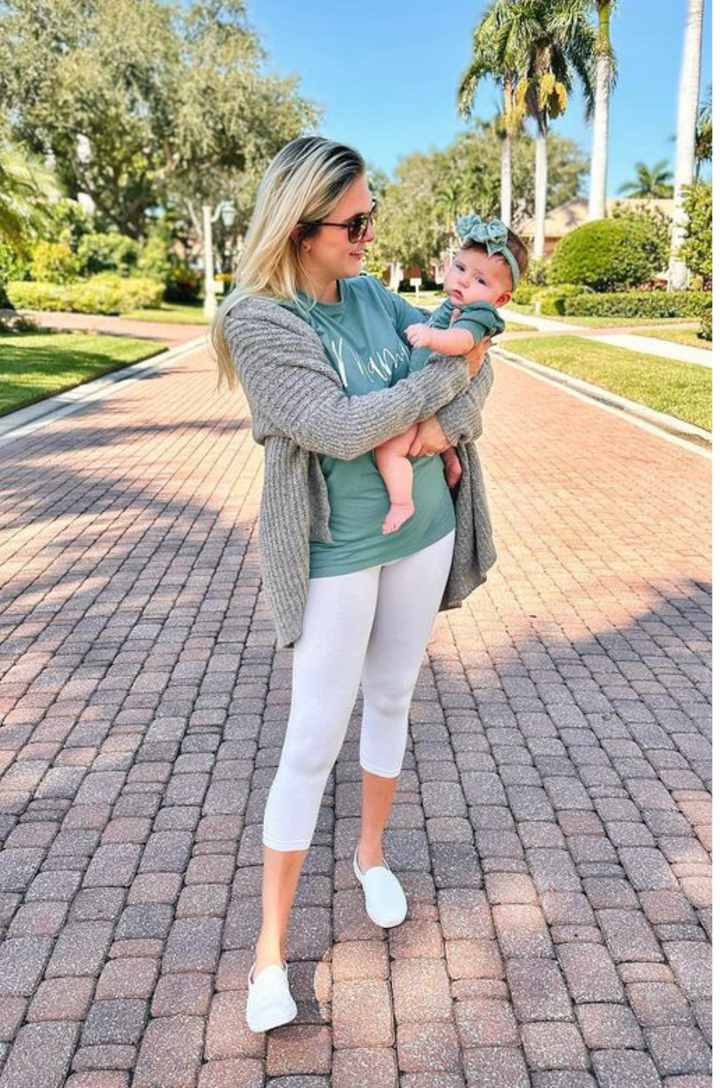 Matching adult and baby medium forest green shirt and onesie with cursive “mama” and “mini” lettering shown together.