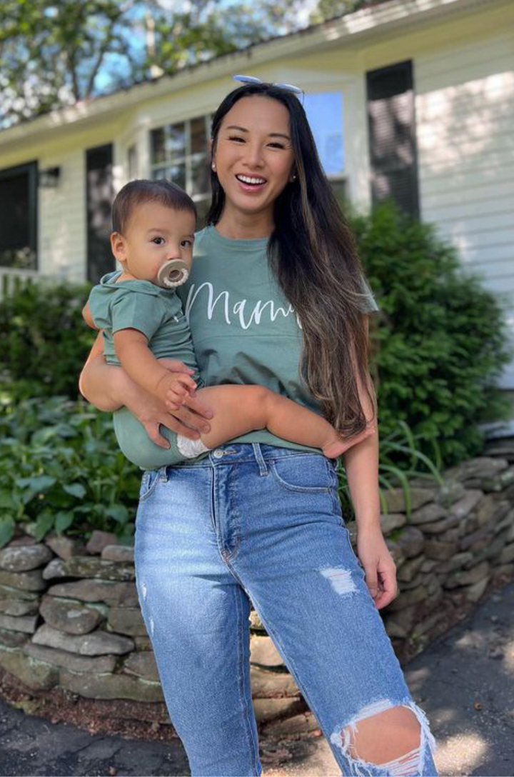 Breastfeeding mom and baby wearing matching medium forest green outffits with cursive “mama” and “mini” text.