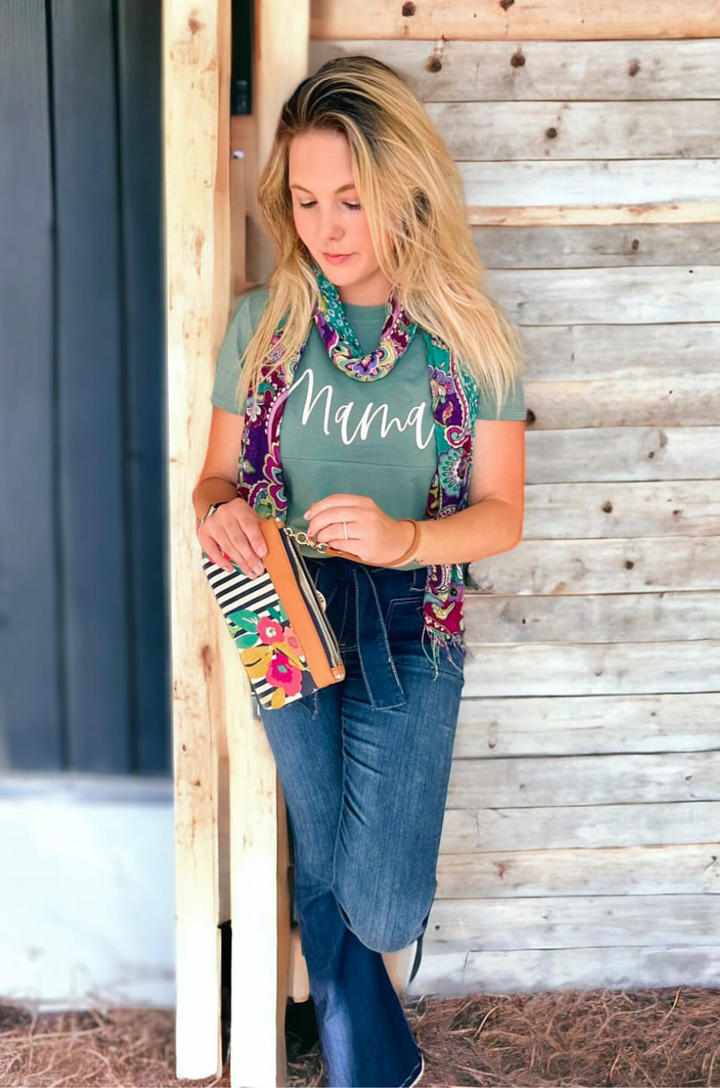 Close-up of cursive “mama” text on medium forest green nursing shirt, styled with a scarf. 
