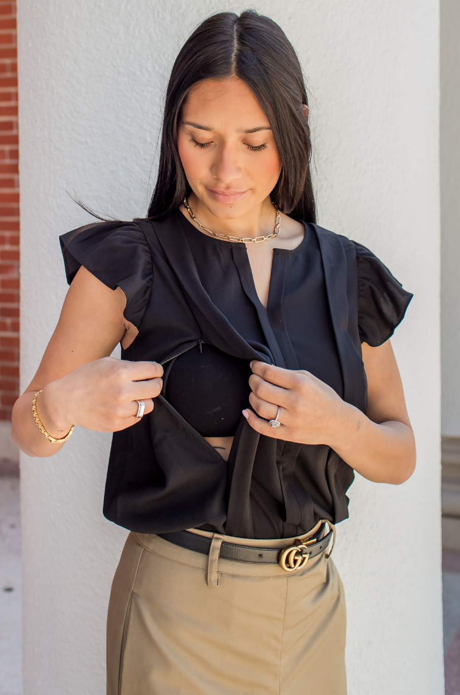 Woman wearing a black nursing top with hidden breastfeeding access and tan pants.