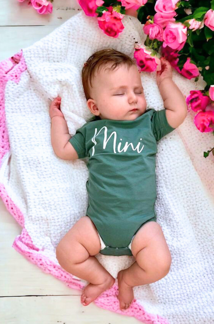 Close-up of cursive “mini” text on matching baby shirt in green.