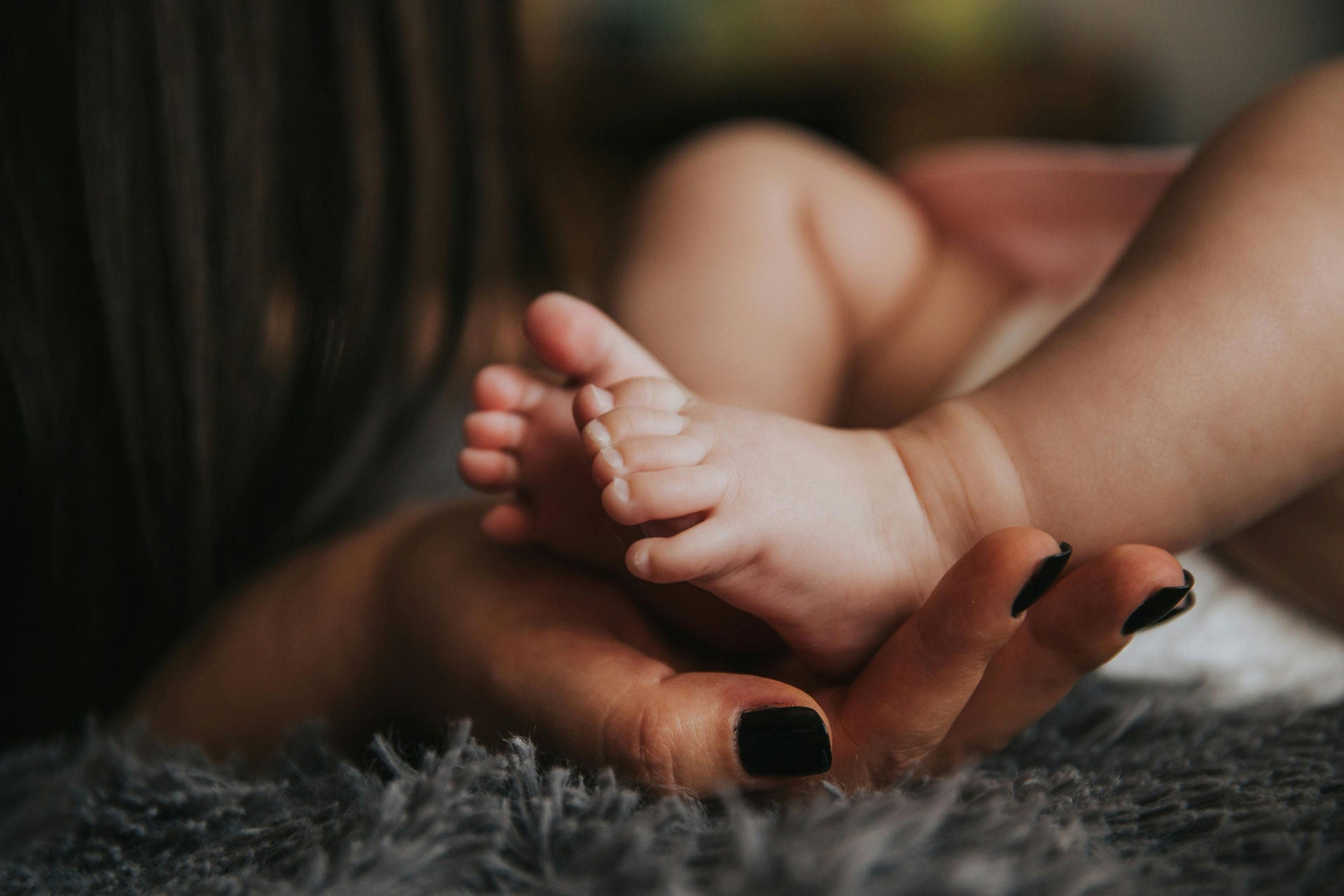 mom with black nails holding baby’s toes