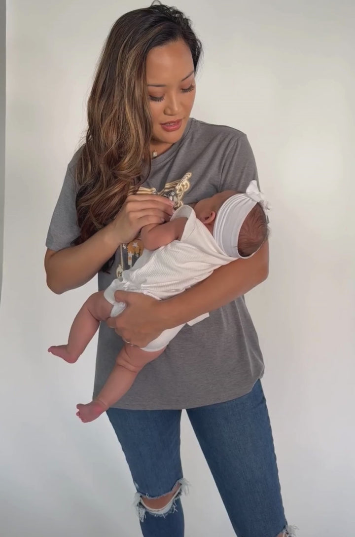 A video shows a mom nursing her baby while wearing the Nashville nursing graphic gray t-shirt with hidden breastfeeding access.