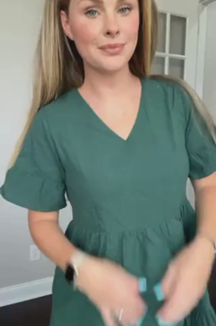 A video demonstrates how a mom uses the hidden breastfeeding zipper access on the Nursing Queen green bell sleeve nursing dress with pockets while showing its flowing movement and fit.