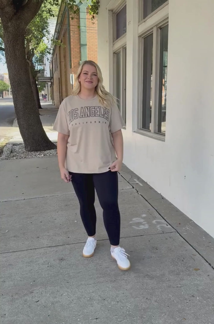 A video shows a mom demonstrating how the hidden zipper breastfeeding access works on the Nursing Queen Los Angeles California tan graphic t-shirt for nursing and pumping.