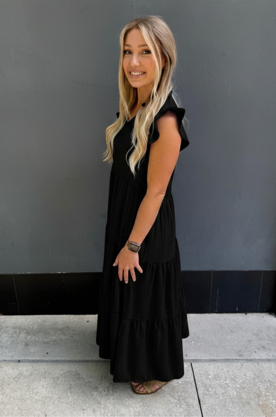 Woman wearing a black nursing dress standing against a gray wall.