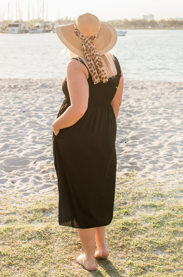Back view of smocked nursing maxi dress worn by model, styled with a hat. 