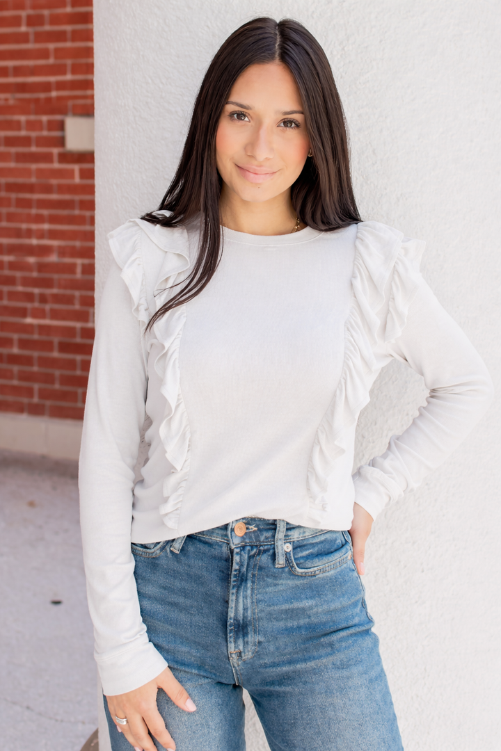 Front view of white ribbed breastfeeding top with ruffle shoulder detail, featuring hidden zipper nursing  access concealed behind the ruffles.