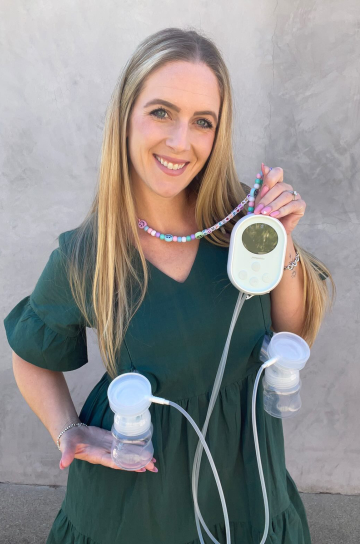 A mom uses her breast pump through the hidden breastfeeding access of the green bell sleeve dress with pockets.